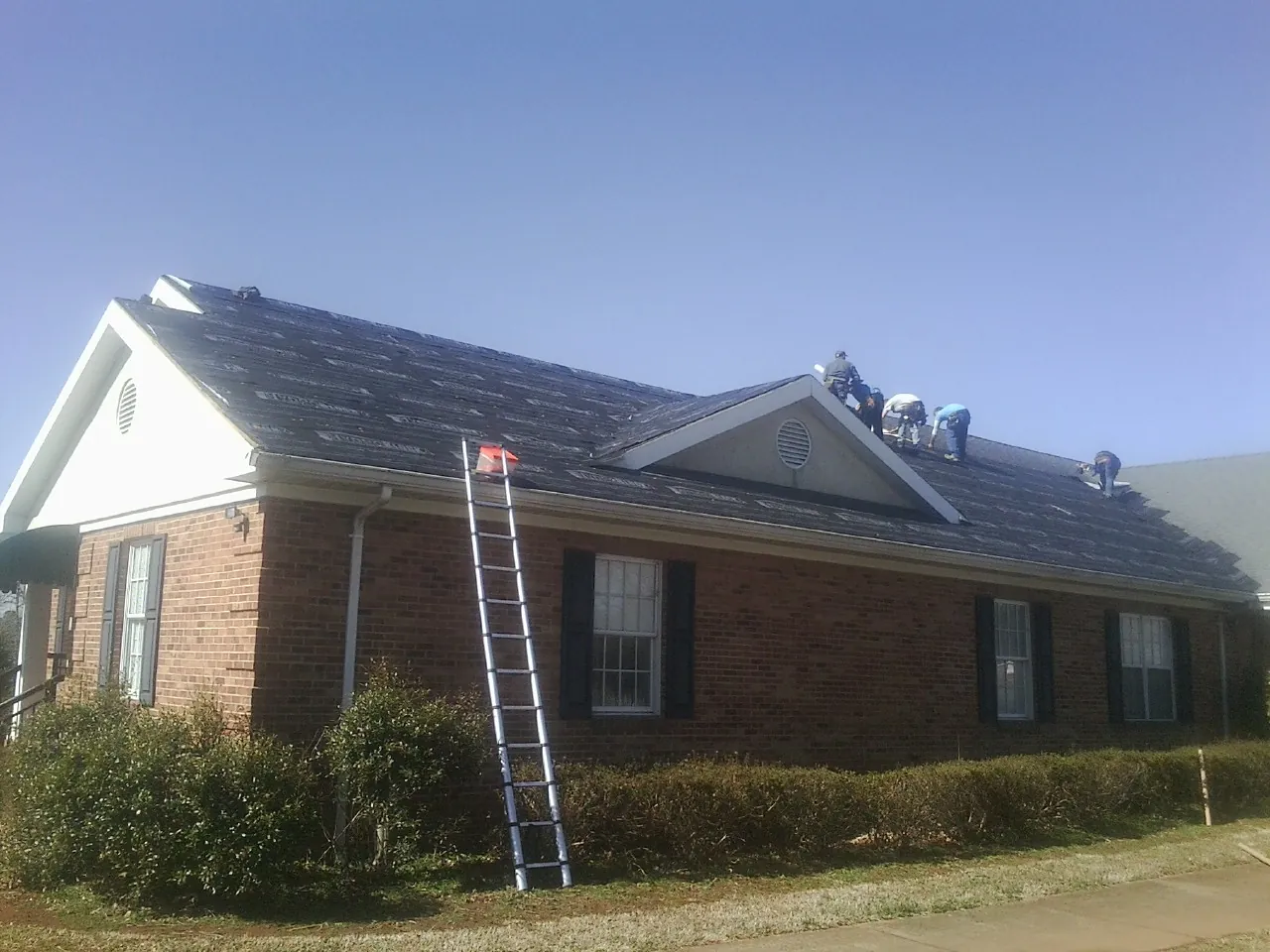 Crew tearing shingles off a brick ranch roof with a ladder set — Metal Roof Repair work by our crew in Lansdowne