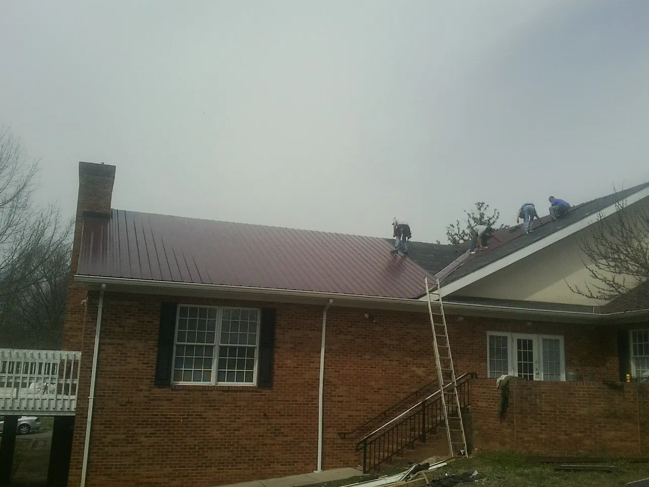 Crew setting red metal roofing panels on a brick home in Lansdowne