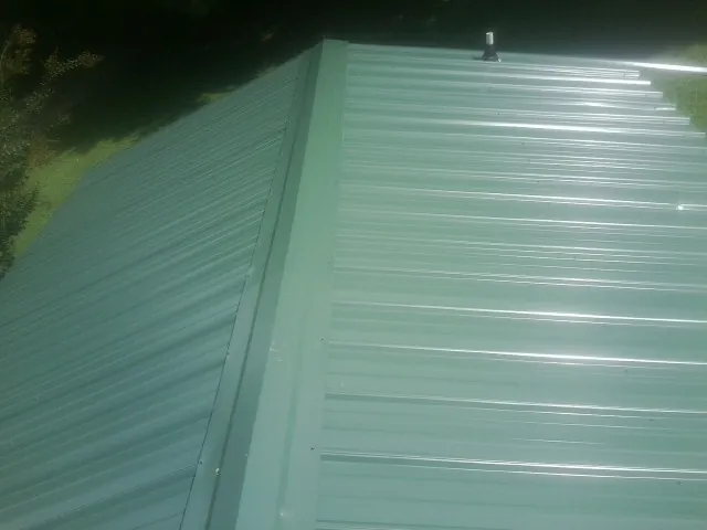 New green metal panels meeting at the ridge of a roof — Flat Roof Repair work by our crew in Lansdowne